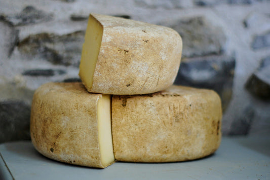 Two rustic wheels of cheese stacked on a surface against a stone wall backdrop