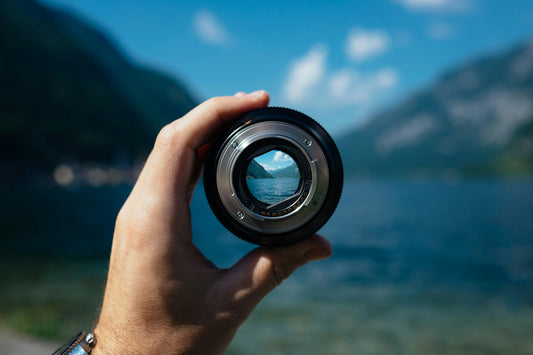 Hand holding a camera lens focusing on a distant mountain lake, highlighting the importance of precise focus and clarity in cognition